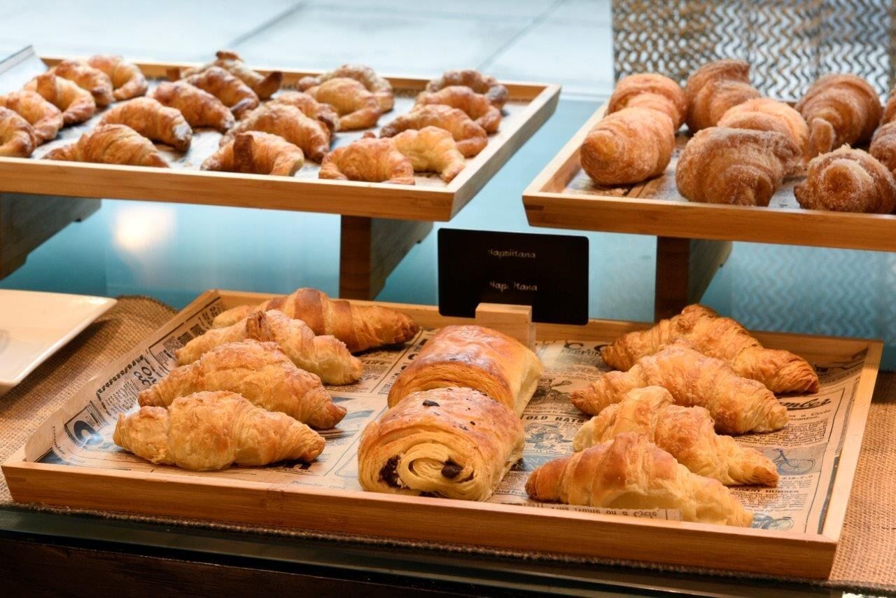 Een presentatie van diverse gebakjes, waaronder croissants en een chocoladerol, gerangschikt op houten dienbladen.