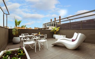A rooftop terrace with white chairs, a dining table, and potted plants.