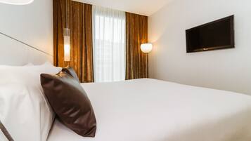 A hotel room with a bed, a TV mounted on the wall, and curtains on the window.