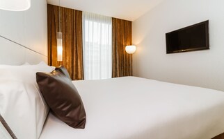 A hotel room with a bed, a TV mounted on the wall, and curtains on the window.