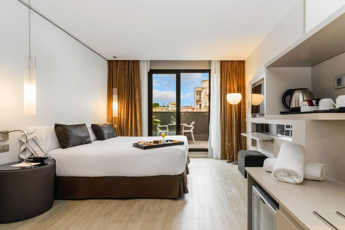 Una habitación de hotel moderna con una cama grande, un escritorio, vistas a la ciudad y un balcón con sillas.