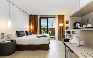 A modern hotel room with a large bed, a desk, a view of the city, and a balcony with chairs. - Grums Hotel (Barcelona)