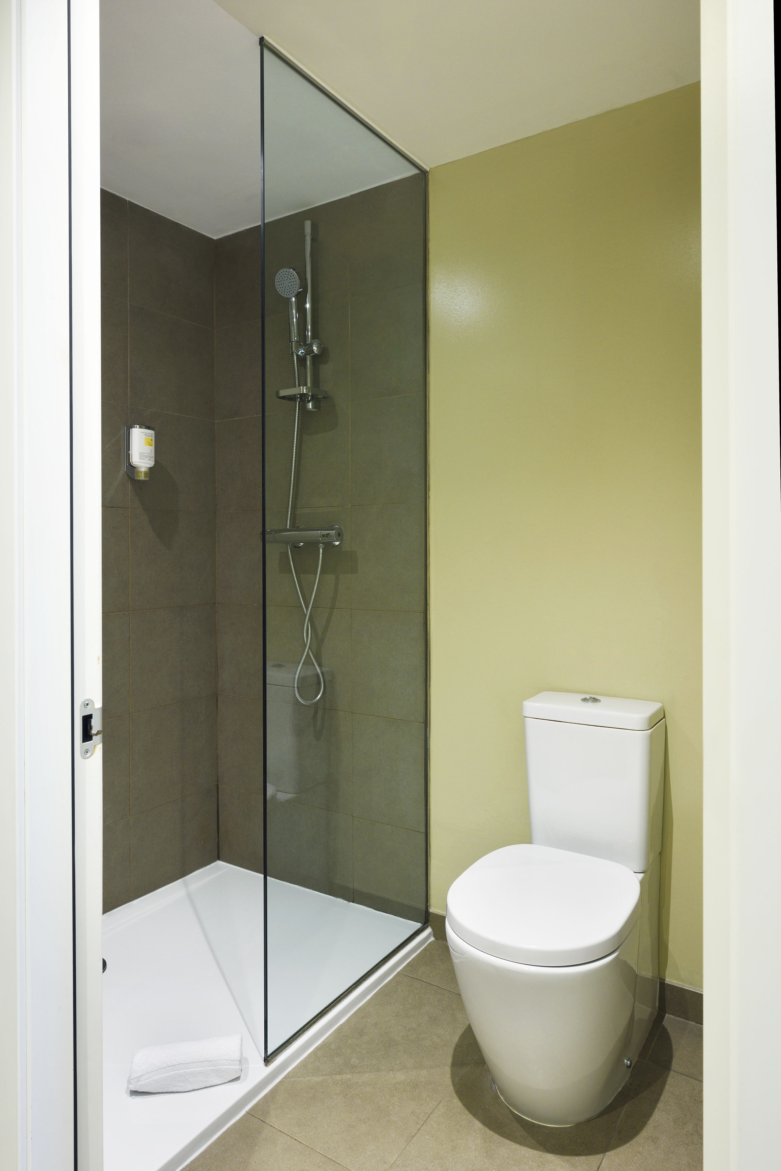 Een badkamer met een douchecabine van glas, een wit toilet en beige tegels.