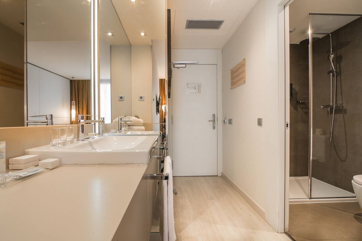 Un baño moderno con un espejo grande, dos lavamanos y una ducha.