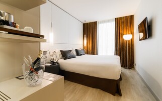 A modern hotel room with a bed, bedside table, and a minibar.