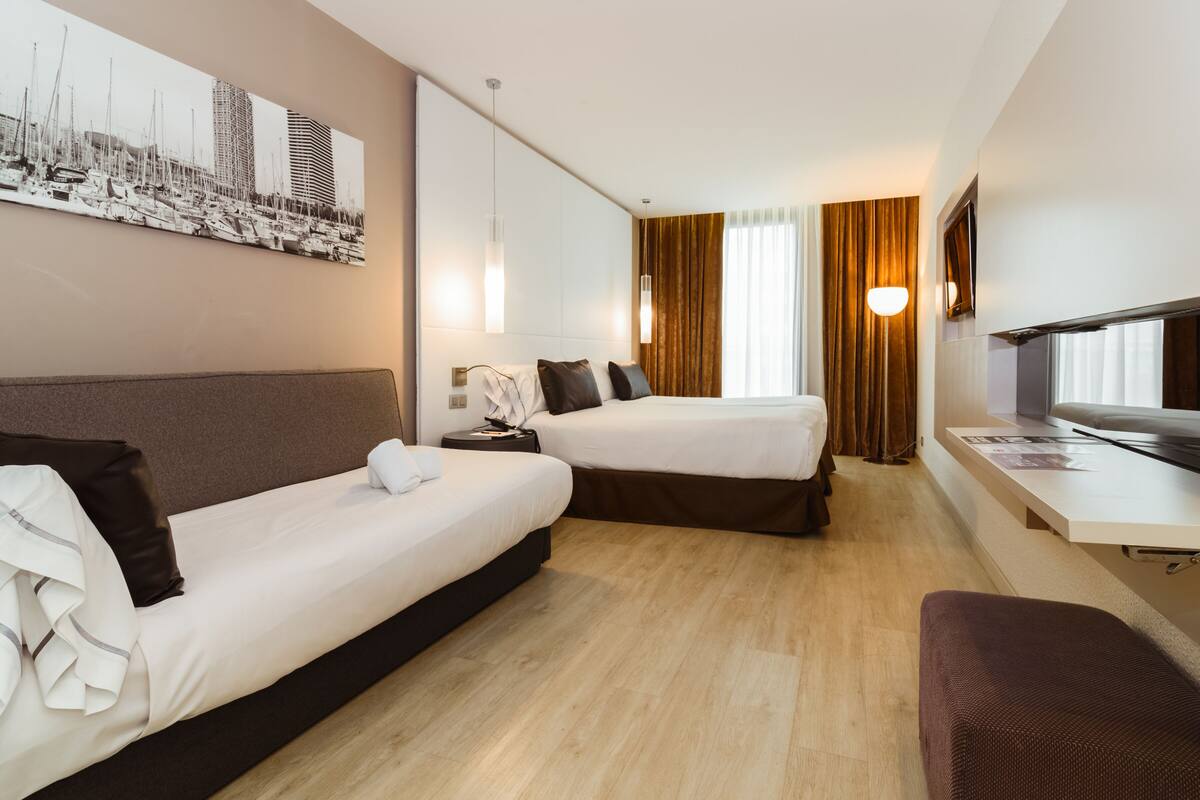 Habitación de hotel con dos camas, un escritorio, un televisor y un ventanal con cortinas.