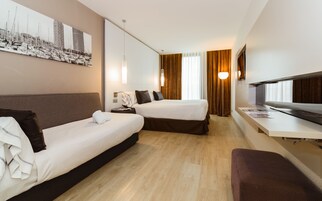 A hotel room with two beds, a desk, a TV, and a large window with curtains.
