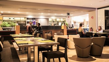 A modern restaurant with multiple seating areas, including tables and booths, and a bar area with a variety of beverages and glasses.