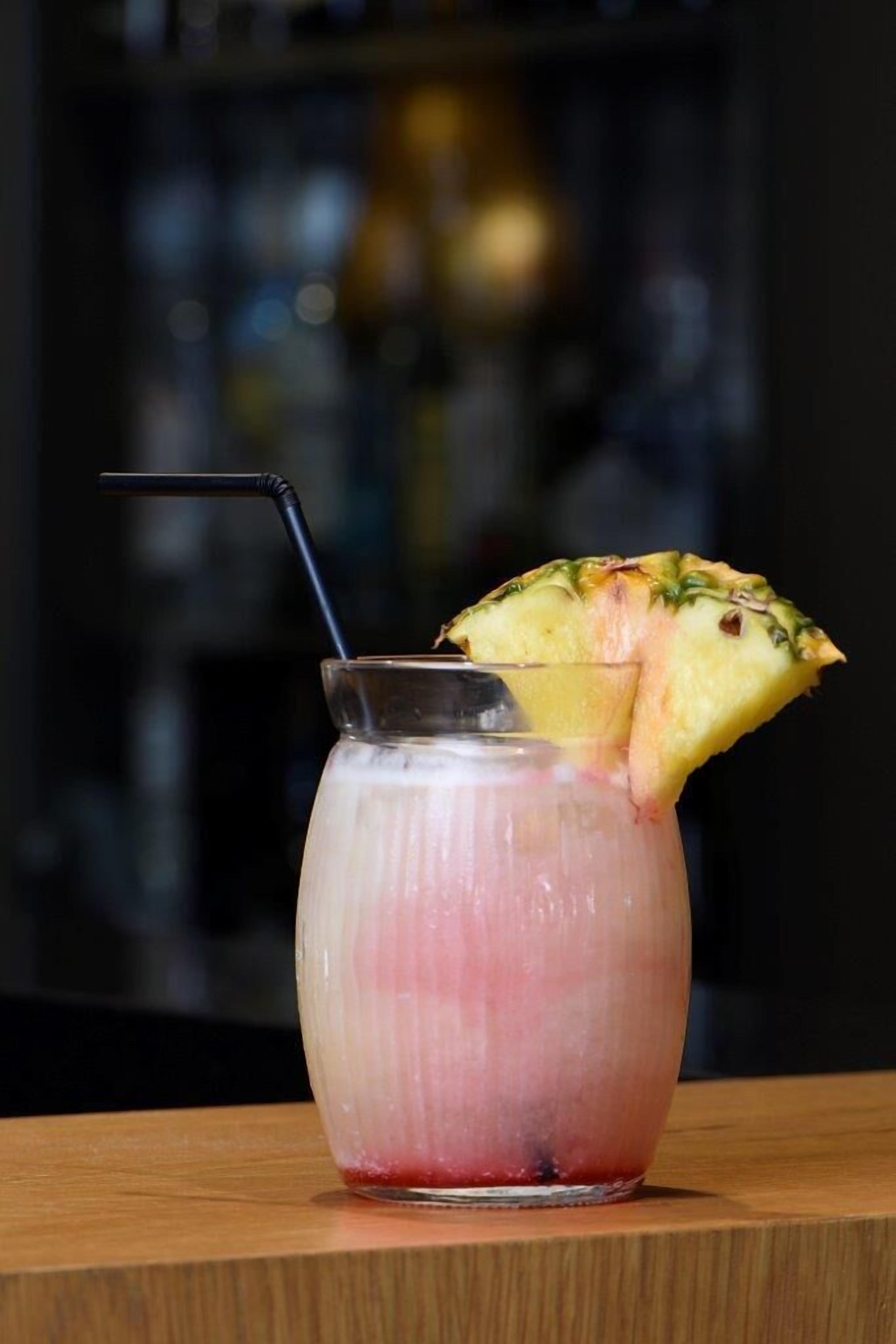 A glass with a straw and a slice of pineapple on the rim, placed on a wooden surface.