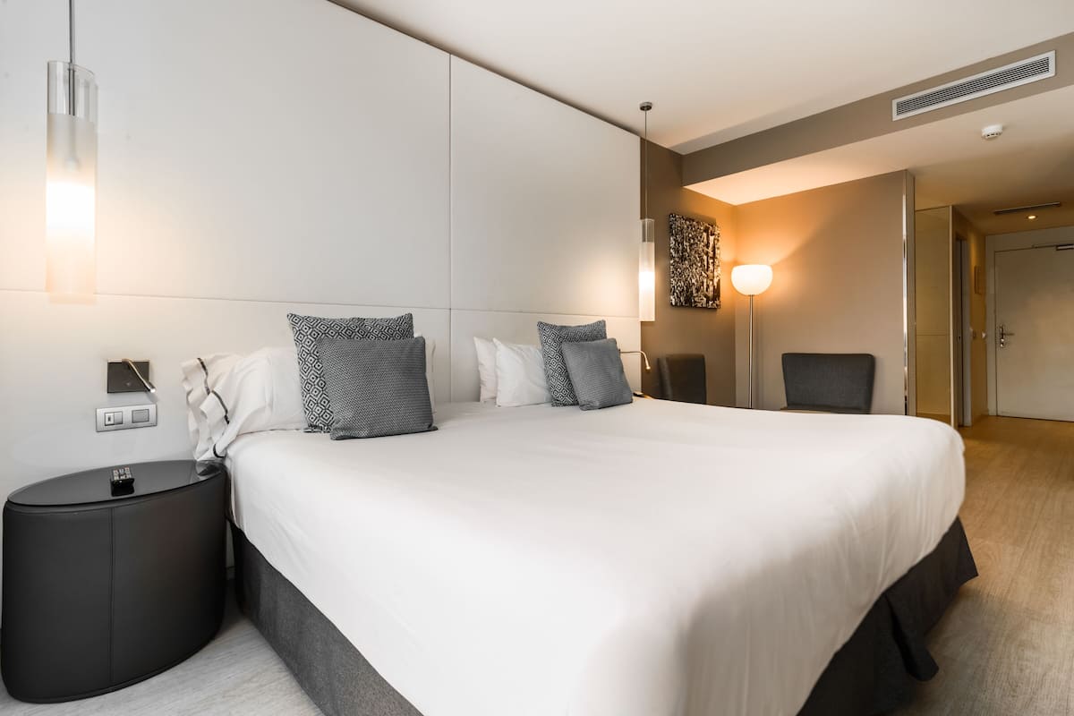 Una habitación de hotel moderna con una cama grande, mesitas de noche, un televisor de pantalla plana y una obra de arte colgada en la pared.
