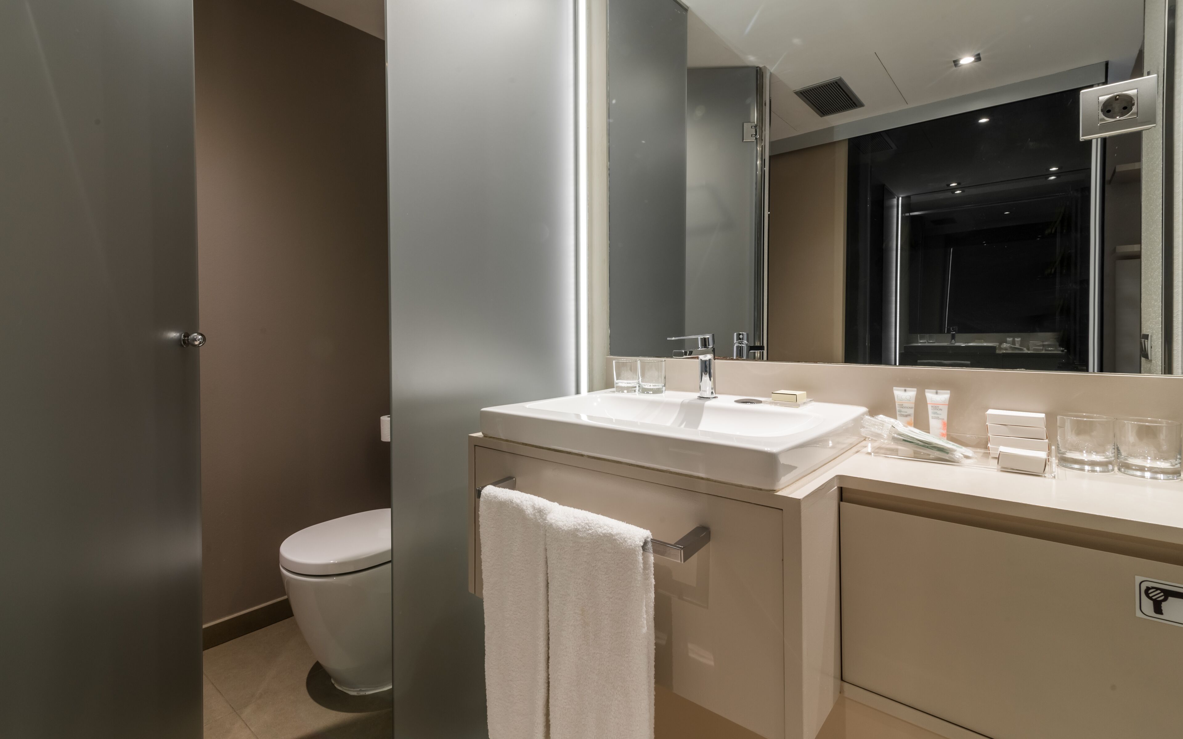 A modern bathroom with a white sink, mirror, and toilet.