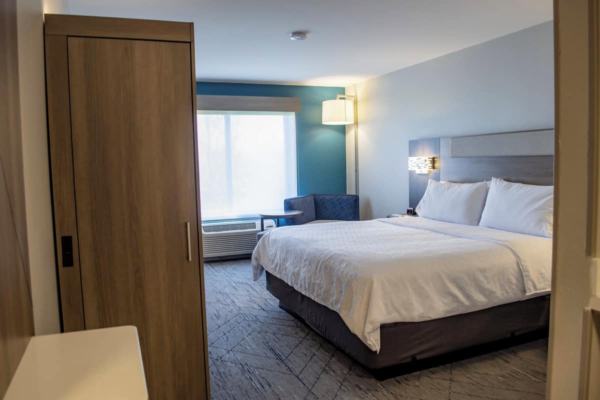 A hotel room with a bed, a desk, a chair, a lamp, and a window.