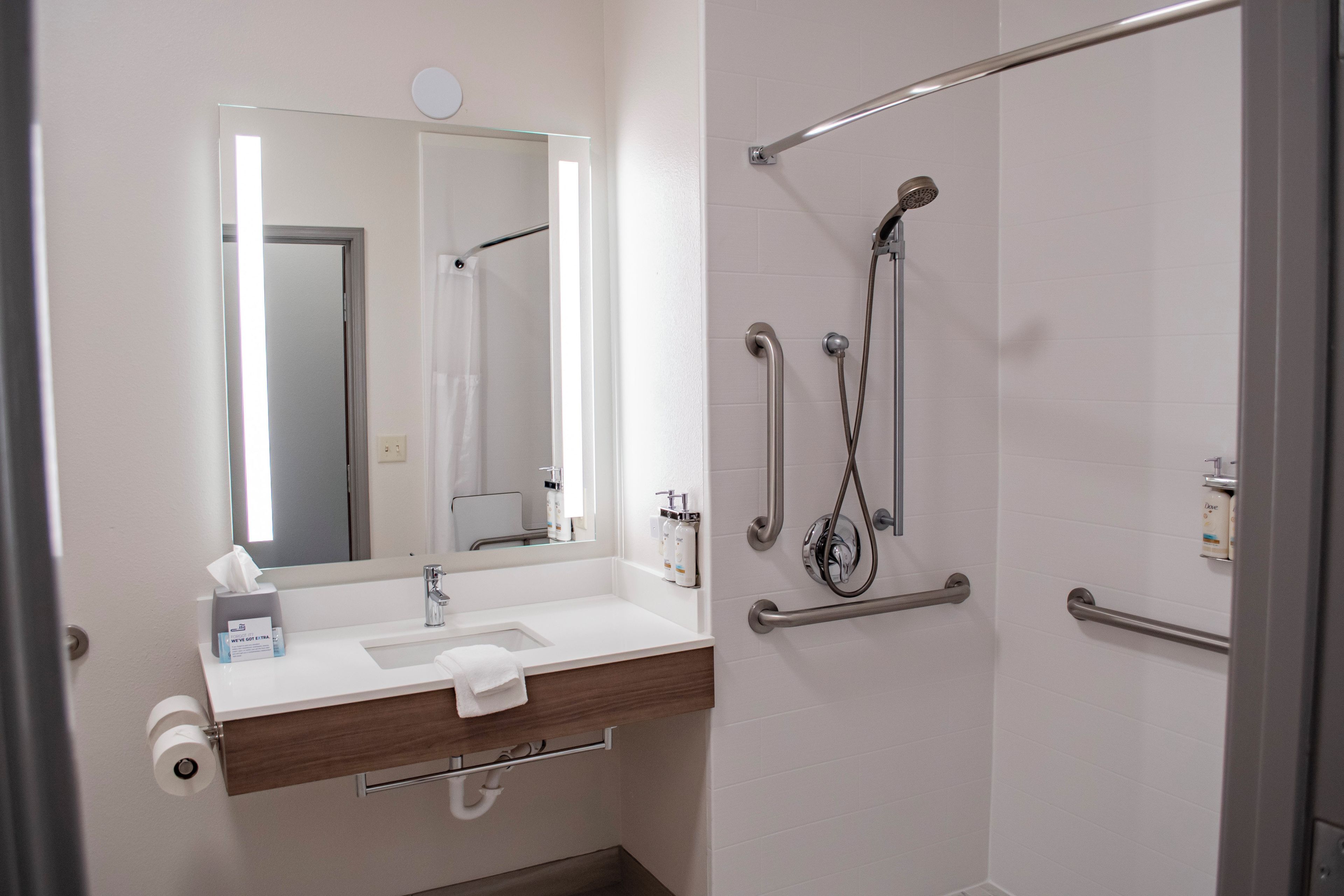 A bathroom with a white sink, a mirror, a towel, and a shower with grab bars.