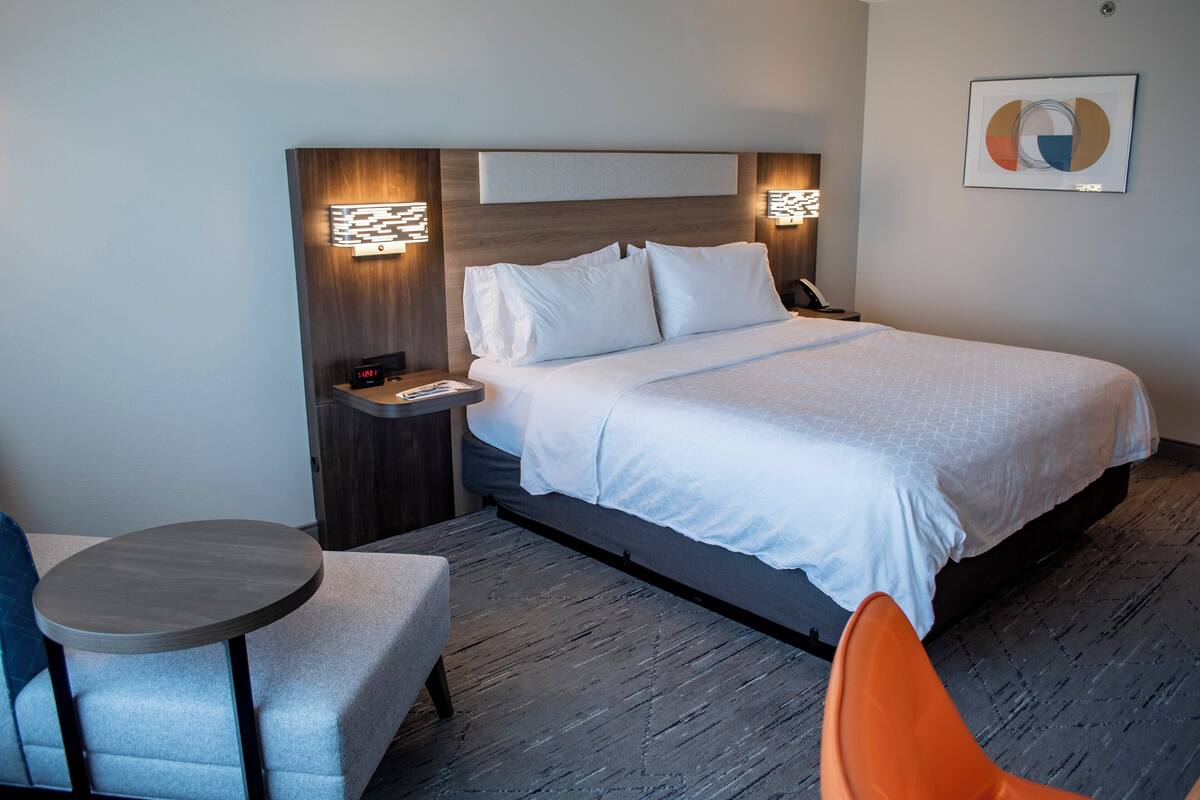 A hotel room with a bed, bedside tables, a round table, and an orange chair.