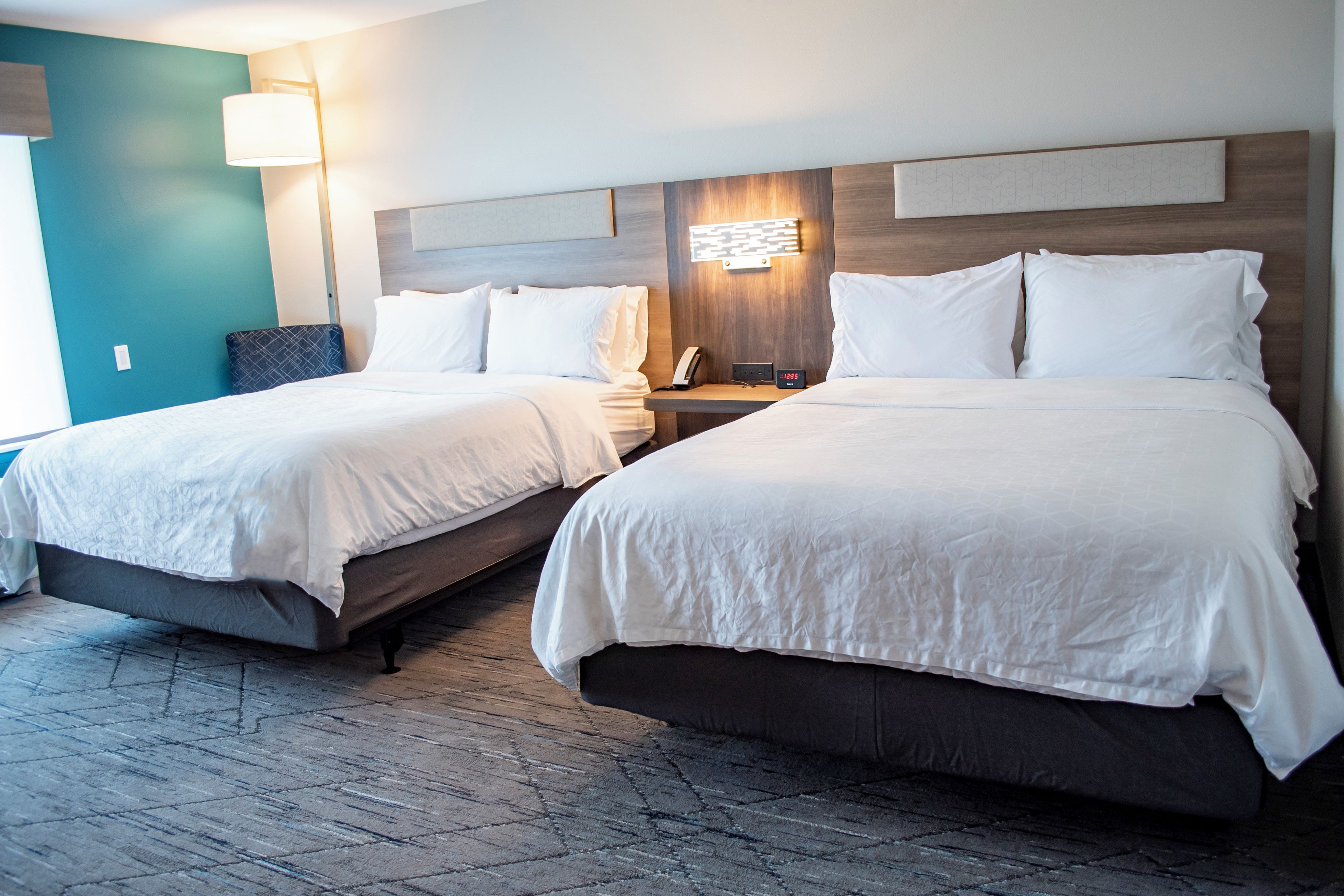 Una habitación de hotel con dos camas, una mesita de noche con lámpara y una lámpara de pared.