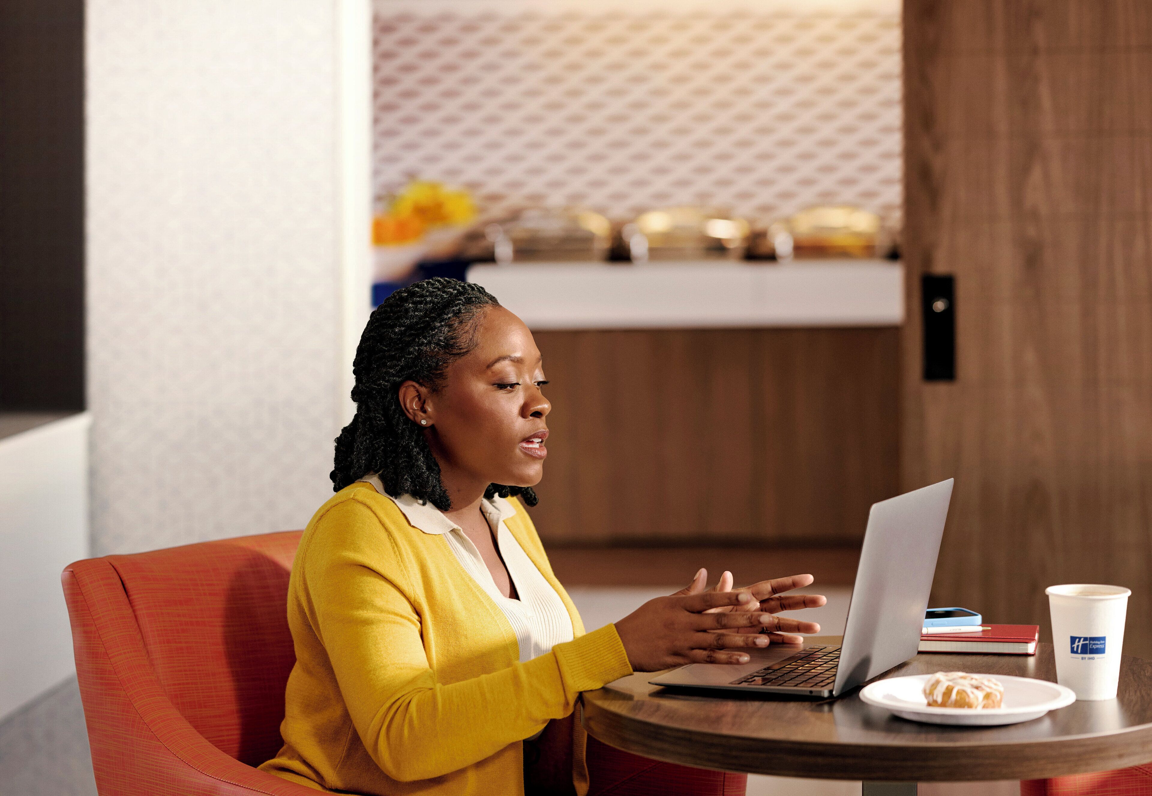 A person sitting at a round table with a laptop, a plate with a pastry, and a coffee cup.