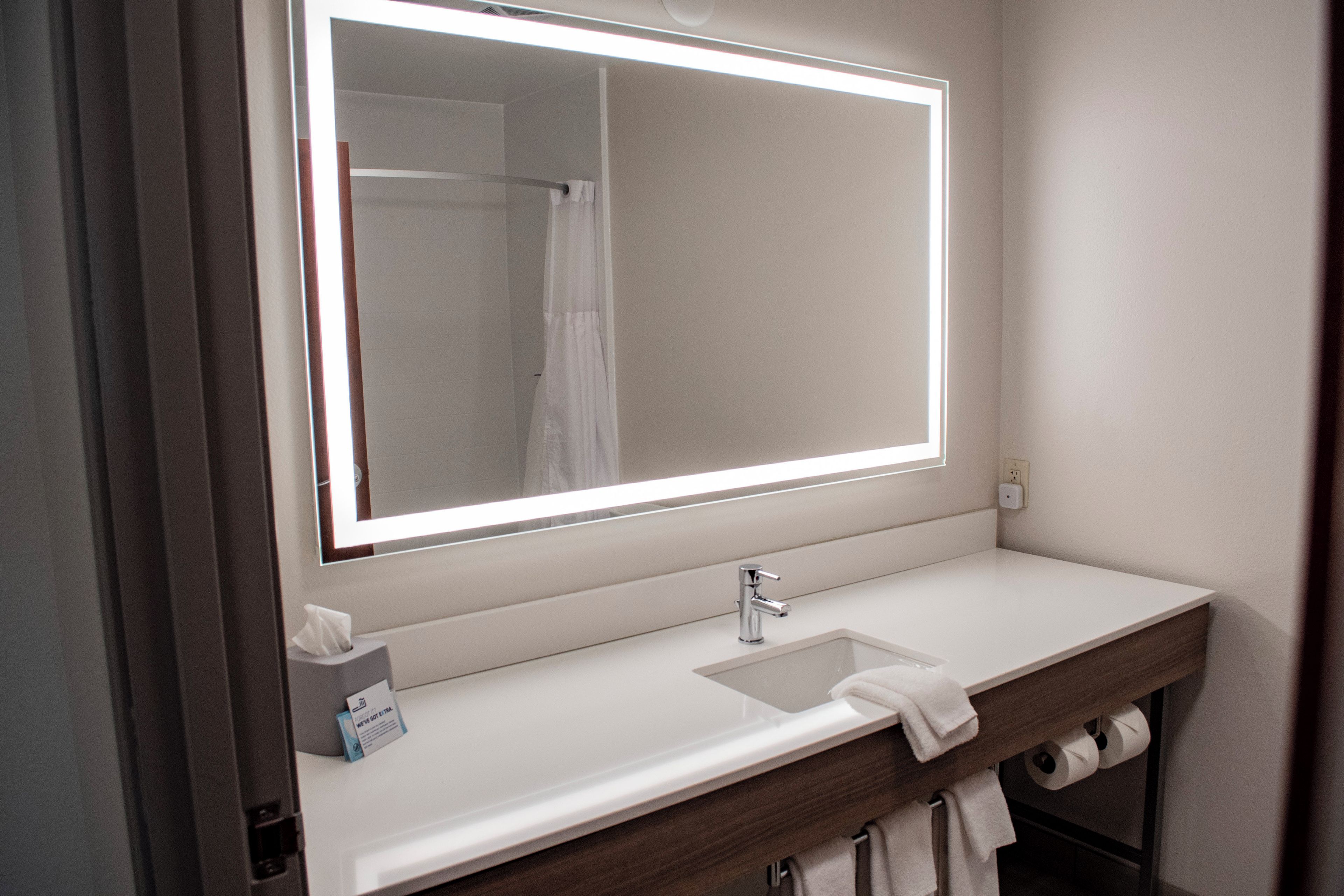 A bathroom with a large mirror, a sink, and a towel rack.
