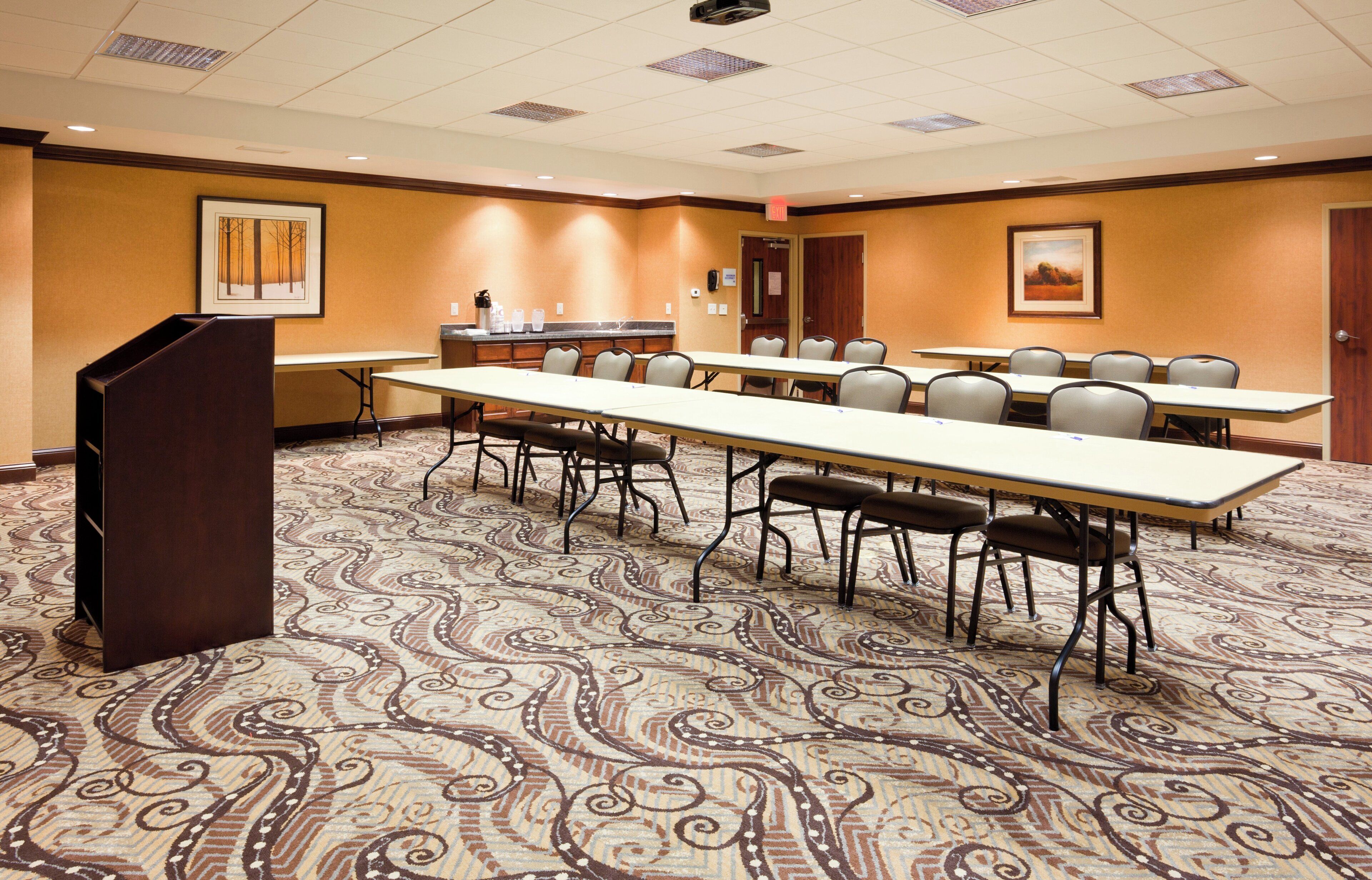 A conference room with a long table, multiple chairs, a podium, and a patterned carpet.
