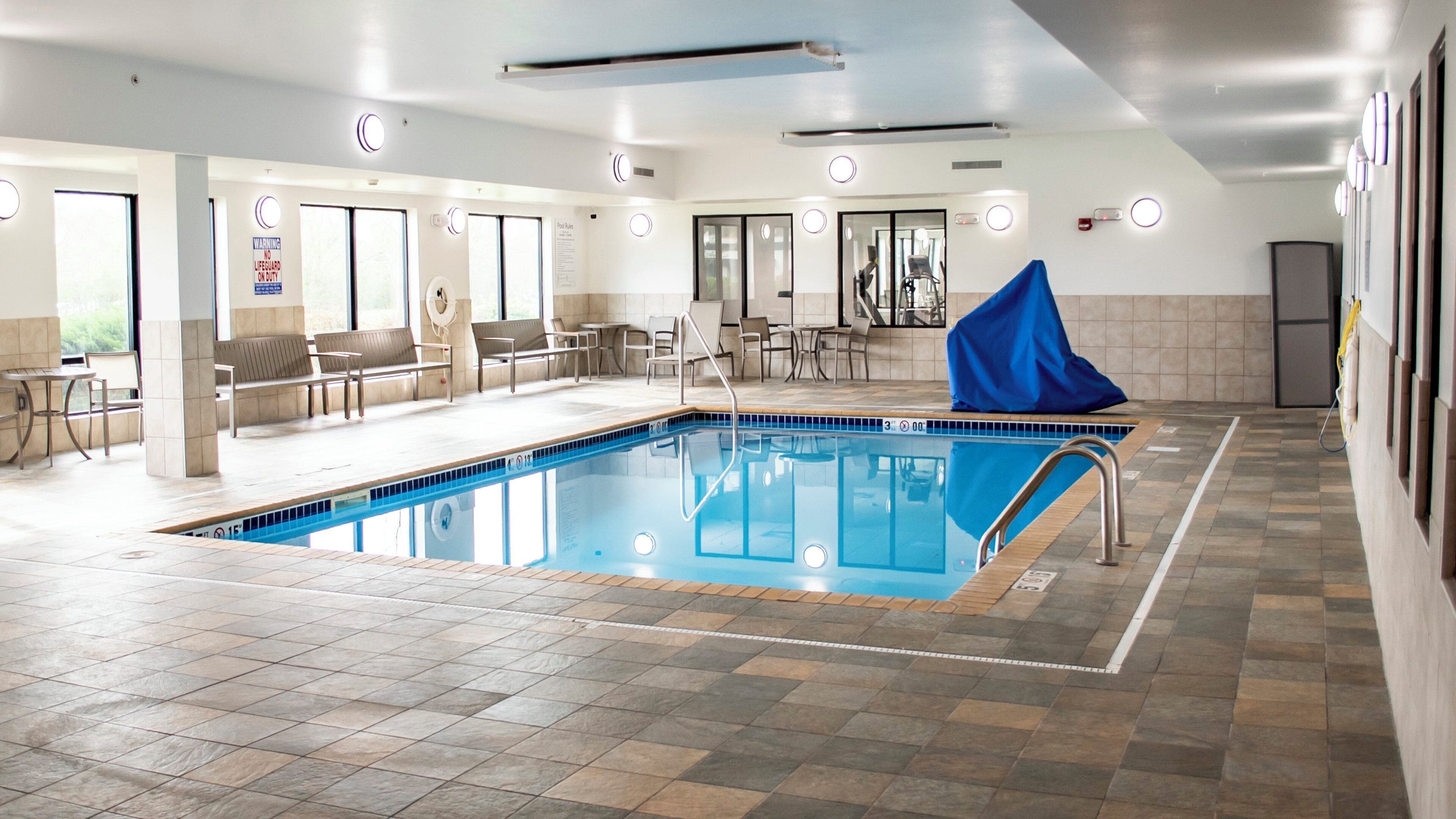 A swimming pool with a blue cover, tiled flooring, and a seating area with chairs and tables.