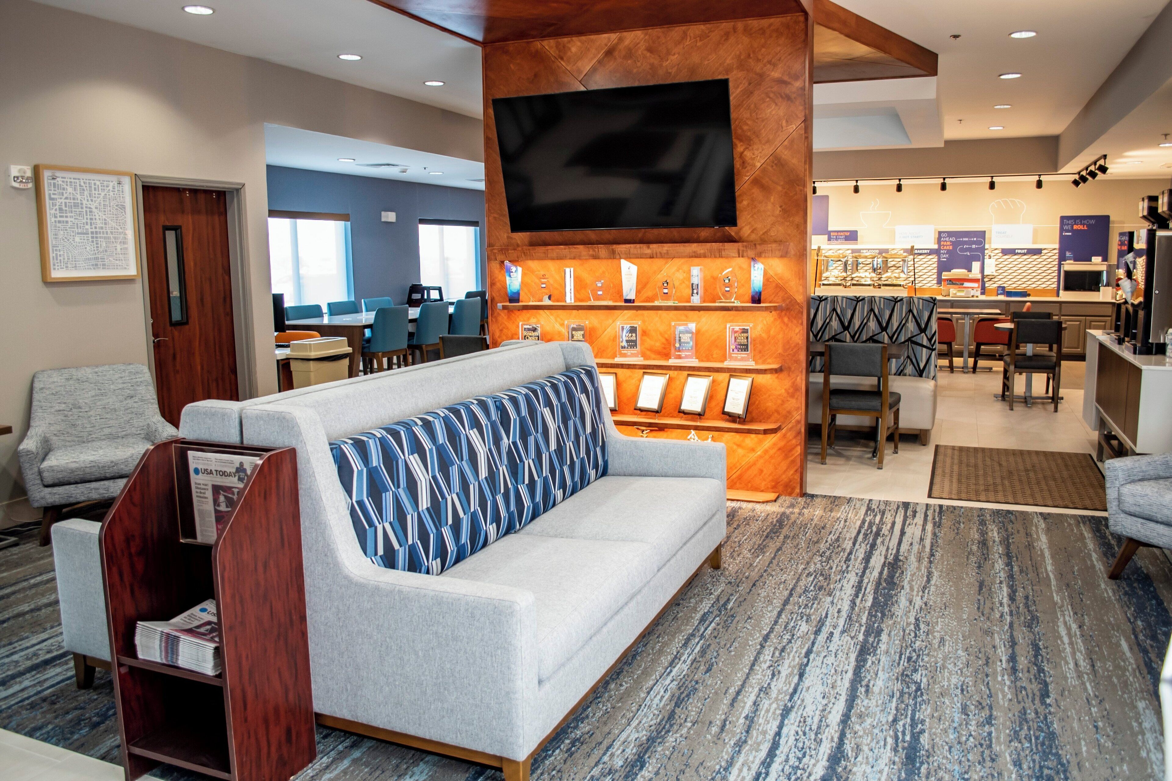 A hotel lobby with a sofa, a television, a reception desk, and a dining area.