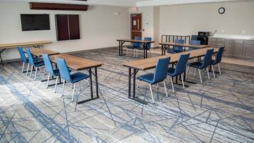 A conference room with tables and chairs, a projector, a clock, and a kitchenette.