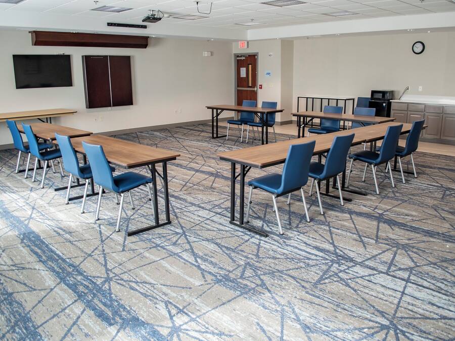 A conference room with tables and chairs, a projector, a clock, and a kitchenette.