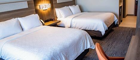 A hotel room with two beds, a desk, a chair, and a wall-mounted light fixture.