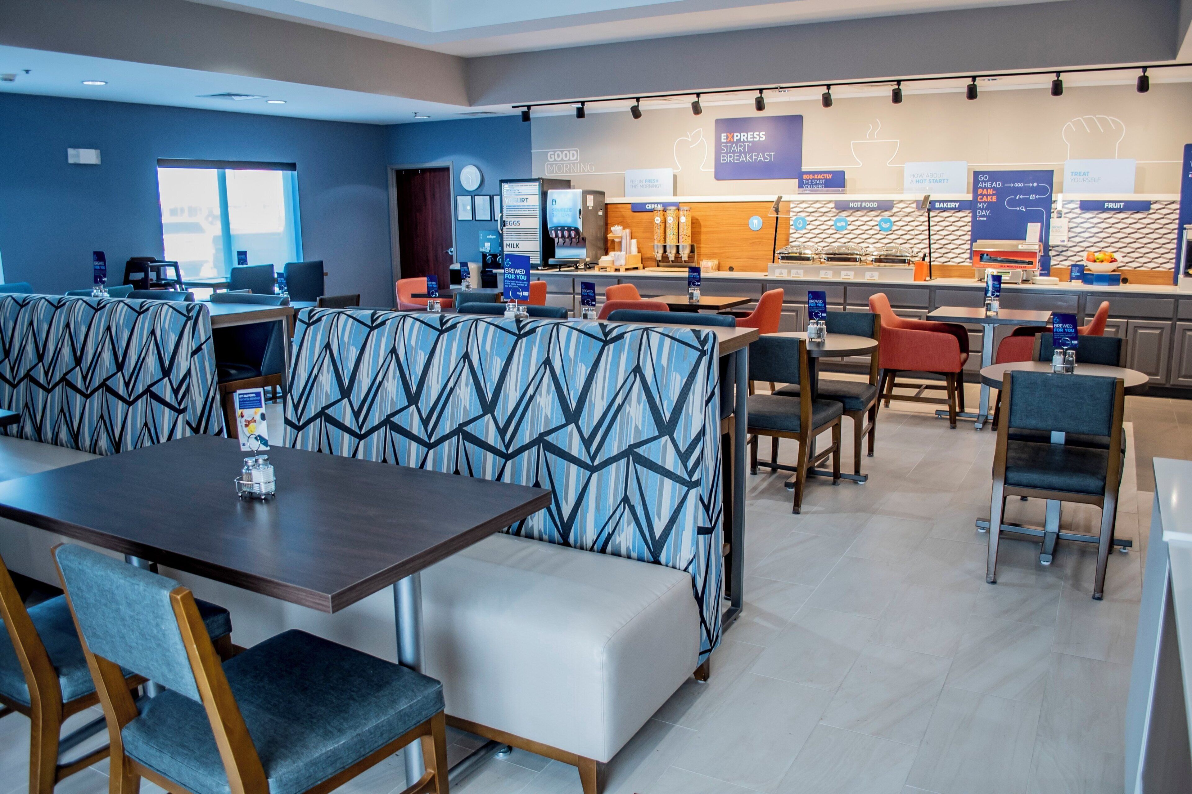A modern hotel dining area with booths, tables, and a breakfast bar.