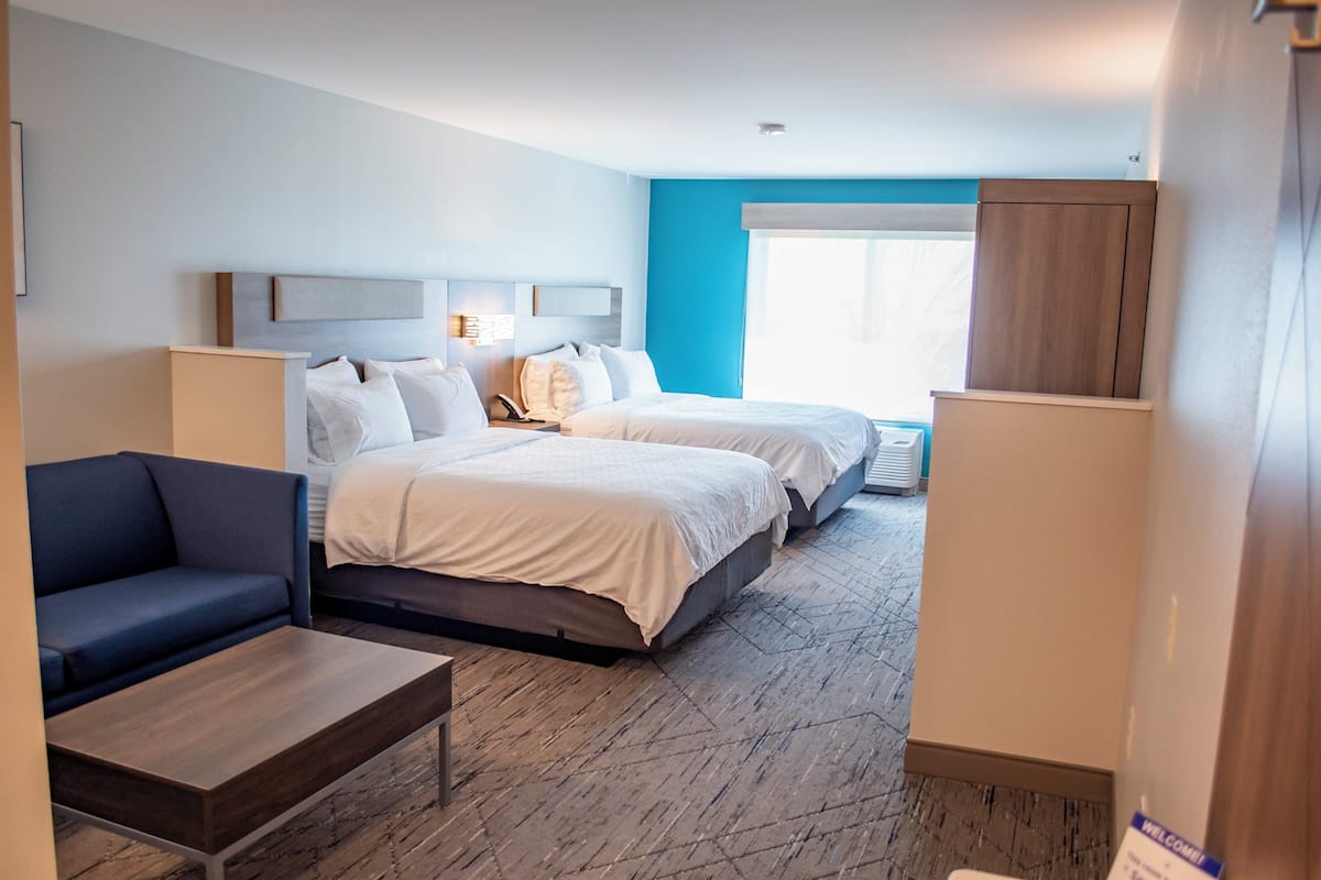 A hotel room with two beds, a sofa, a small table, and a window with a view.