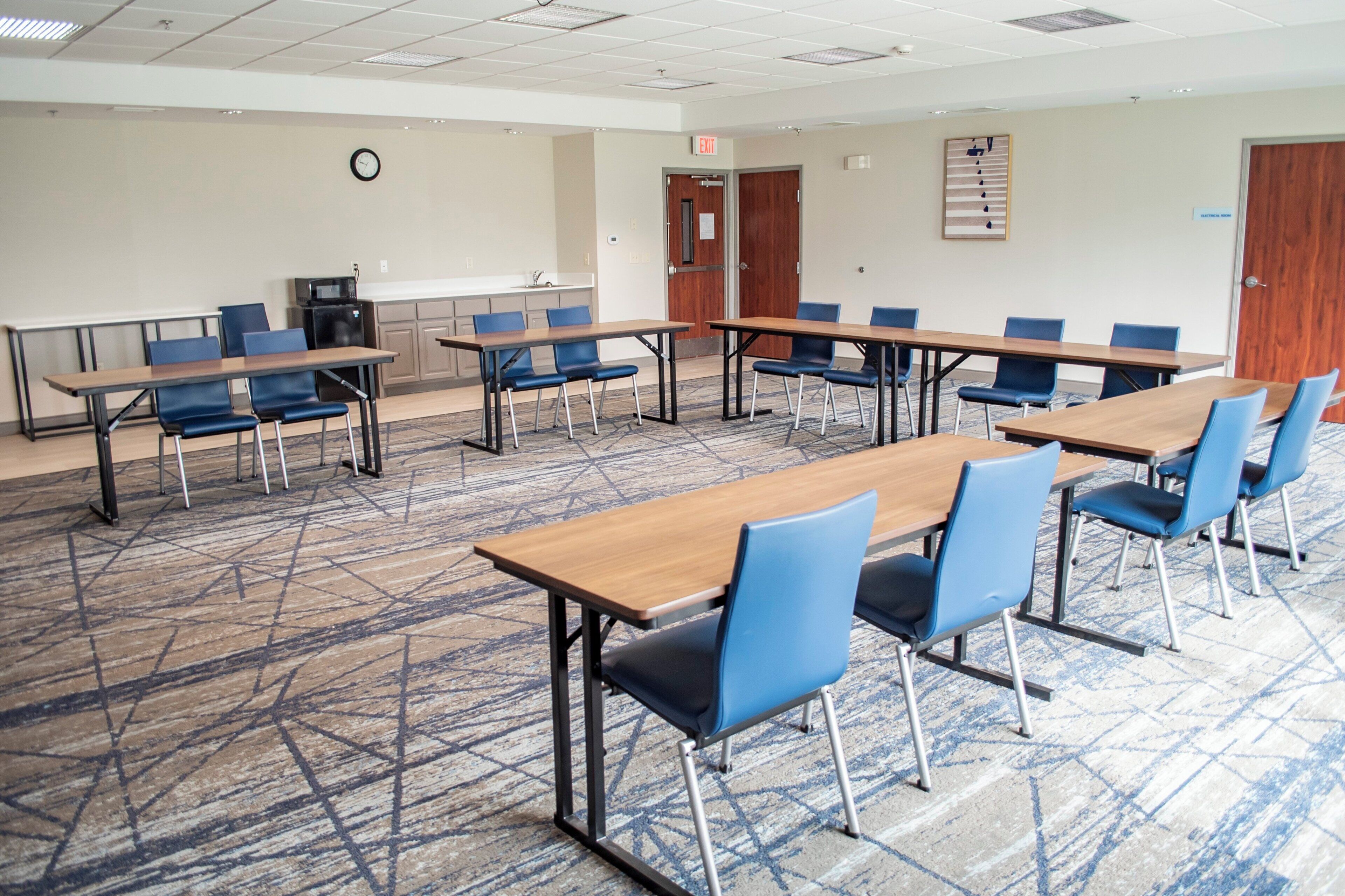 A conference room with multiple tables and chairs, a clock on the wall, and an exit door.