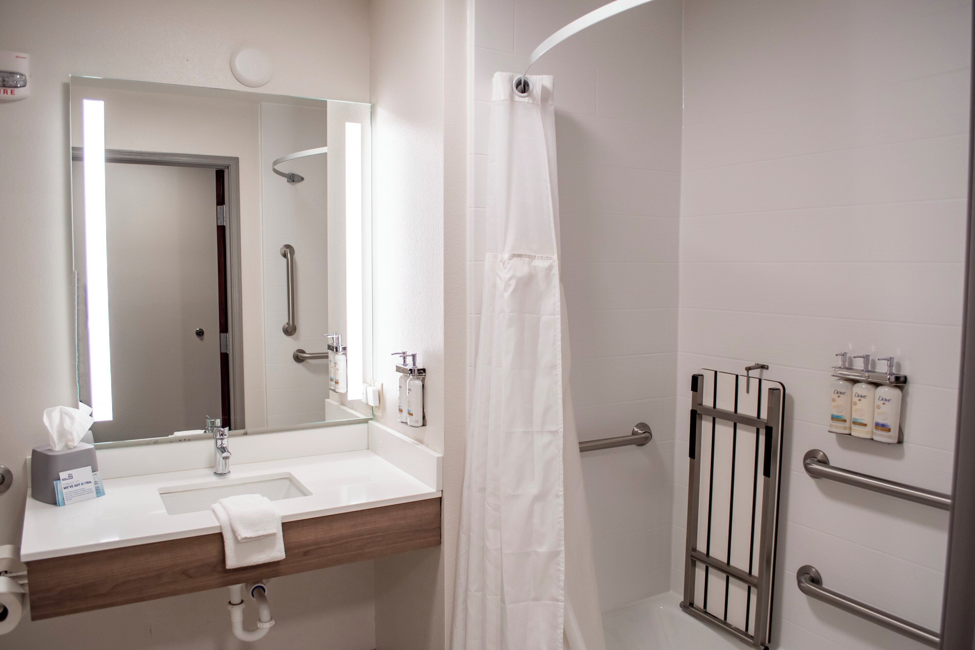 A bathroom with a sink, mirror, shower curtain, and handrails.