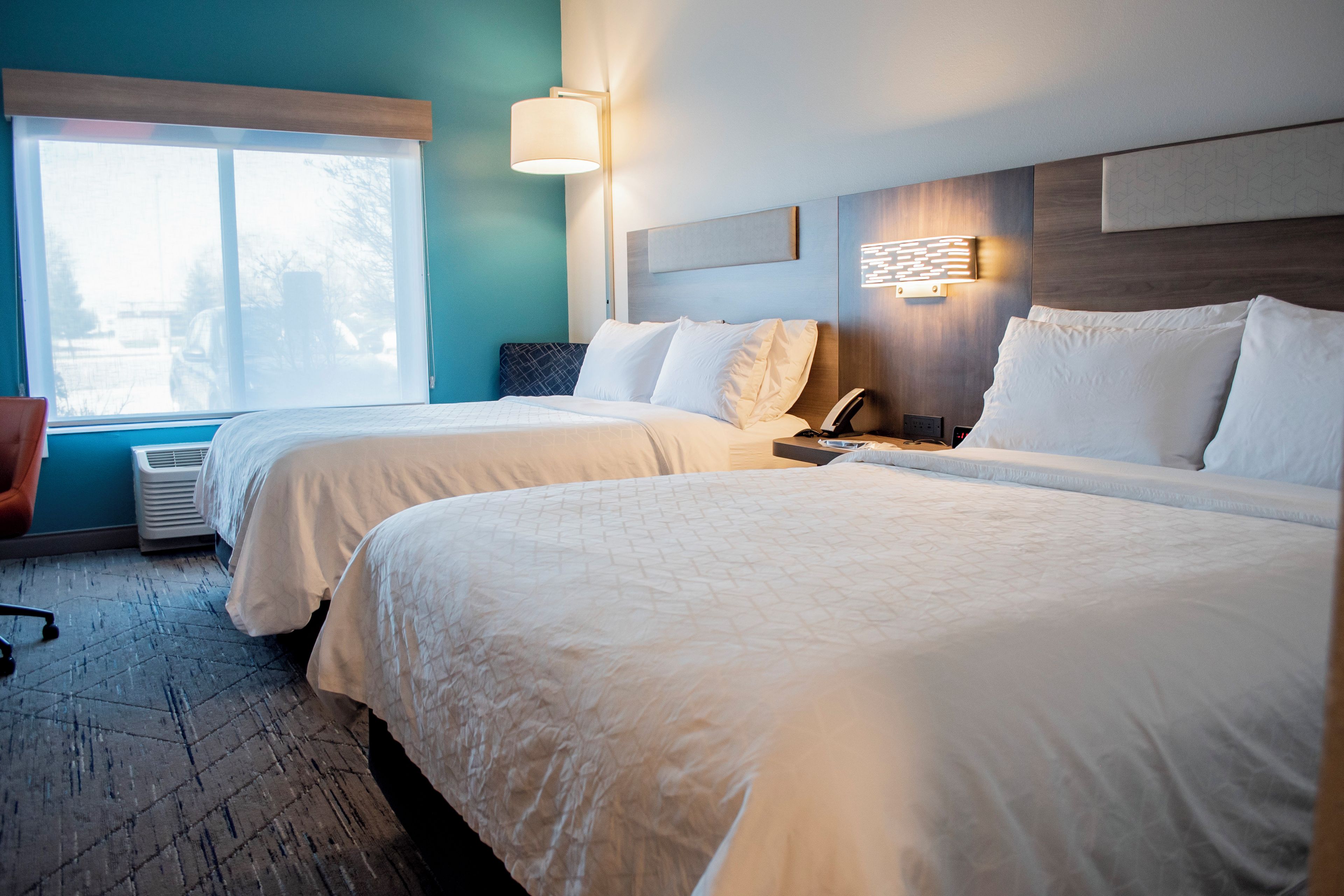 A hotel room with two beds, a window, a wall-mounted phone, and a heater.