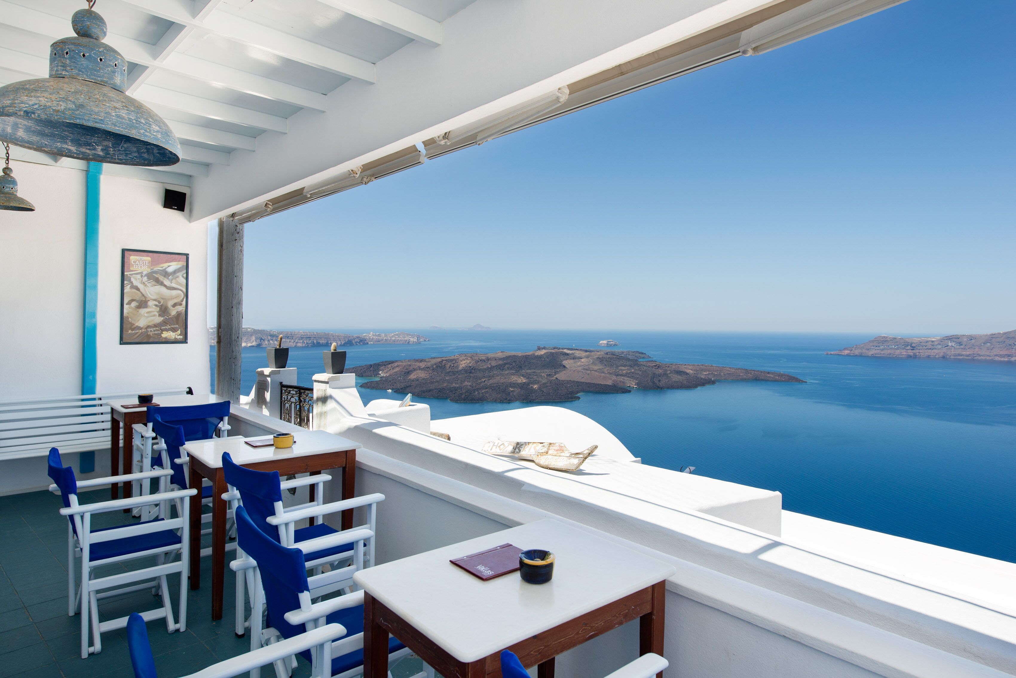 Eine Terrasse mit weiß-blauer Möbelanordnung, Blick auf das Meer und einer blauen Pendelleuchte.