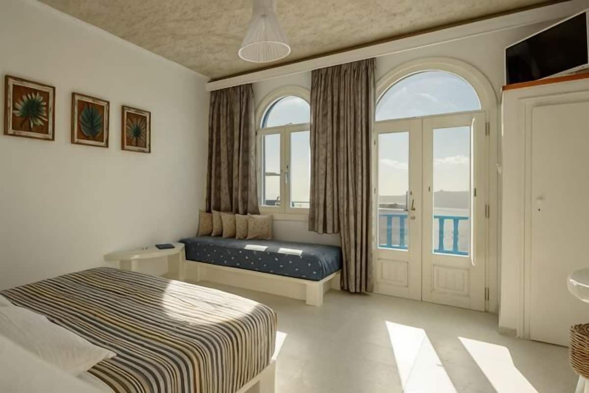 Une chambre à coucher comprenant un lit, un coin salon, une fenêtre avec des rideaux et un balcon.