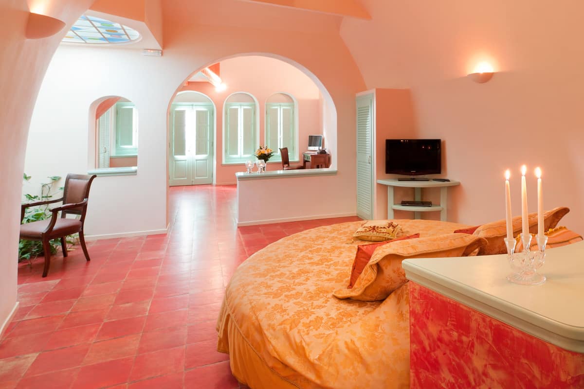Une chambre avec un grand lit, une télévision et un bureau avec une chaise. Il y a une fenêtre donnant sur l’extérieur.