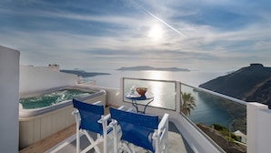 A balcony with a hot tub, blue chairs, and a table with a bowl and glass. - Vallas Apartments & Villas (Santorini)