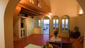 A spacious living area with a high ceiling, wooden beams, and a view of the sea through arched windows. - Vallas Apartments & Villas (Santorini)