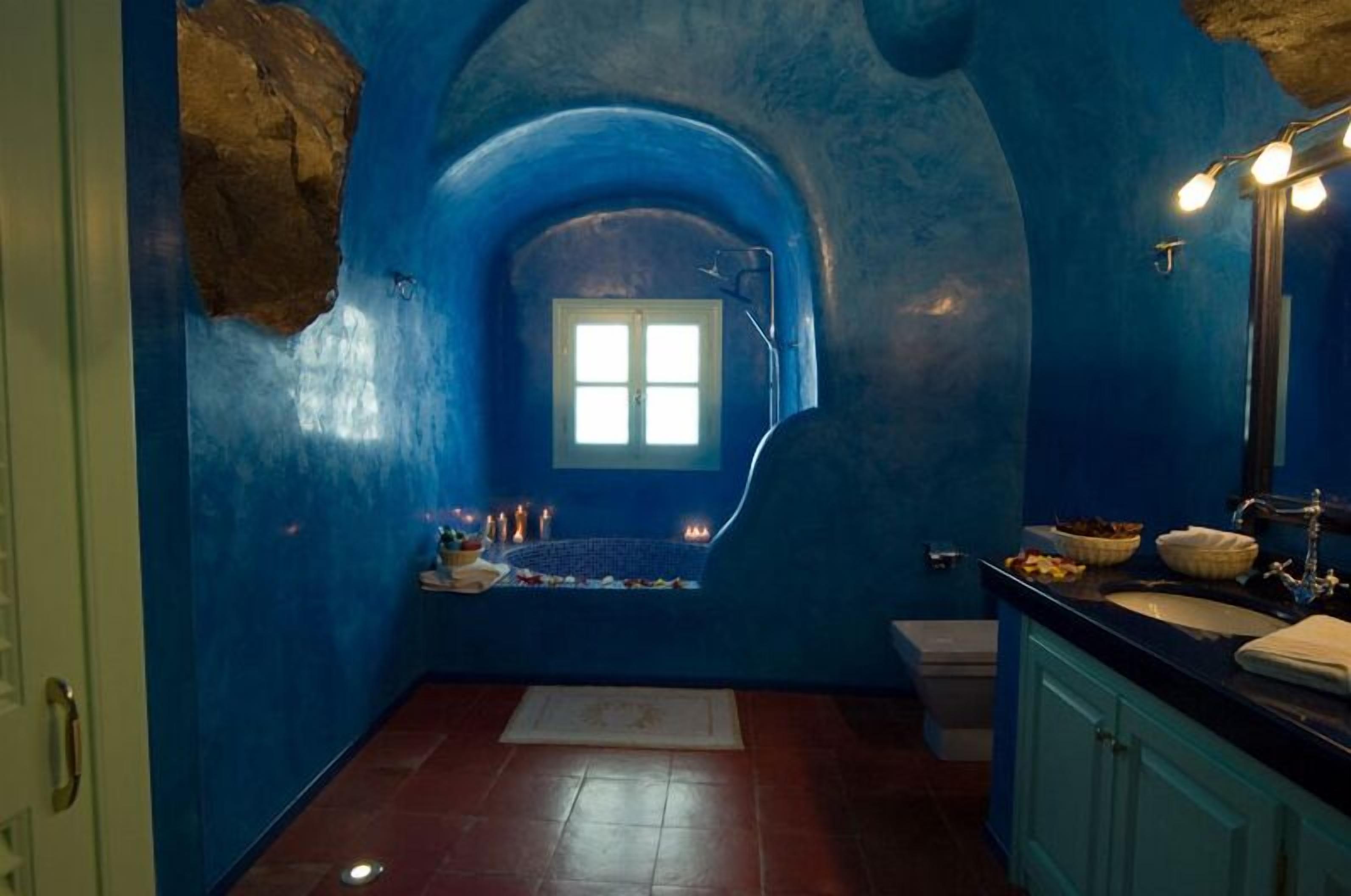 A bathroom with a blue-tiled wall, a window, a sink, and a mirror.