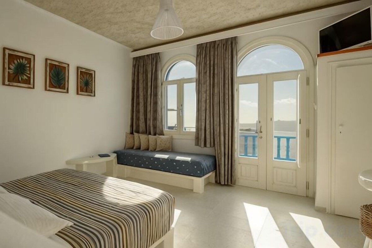Quarto com cama, um assento junto à janela e uma varanda.