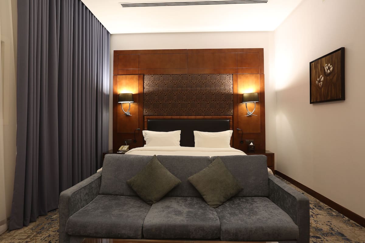 Une chambre d’hôtel comprenant un lit, deux lampes de chevet, un canapé avec des coussins, une table de chevet, une œuvre d’art accrochée au mur et une moquette à motifs.