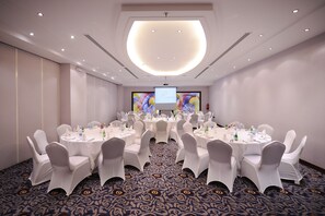 A conference room with round tables, white chairs, and a large screen at the front. - Qaser Alhamra Hotel Riyadh (Riyadh)