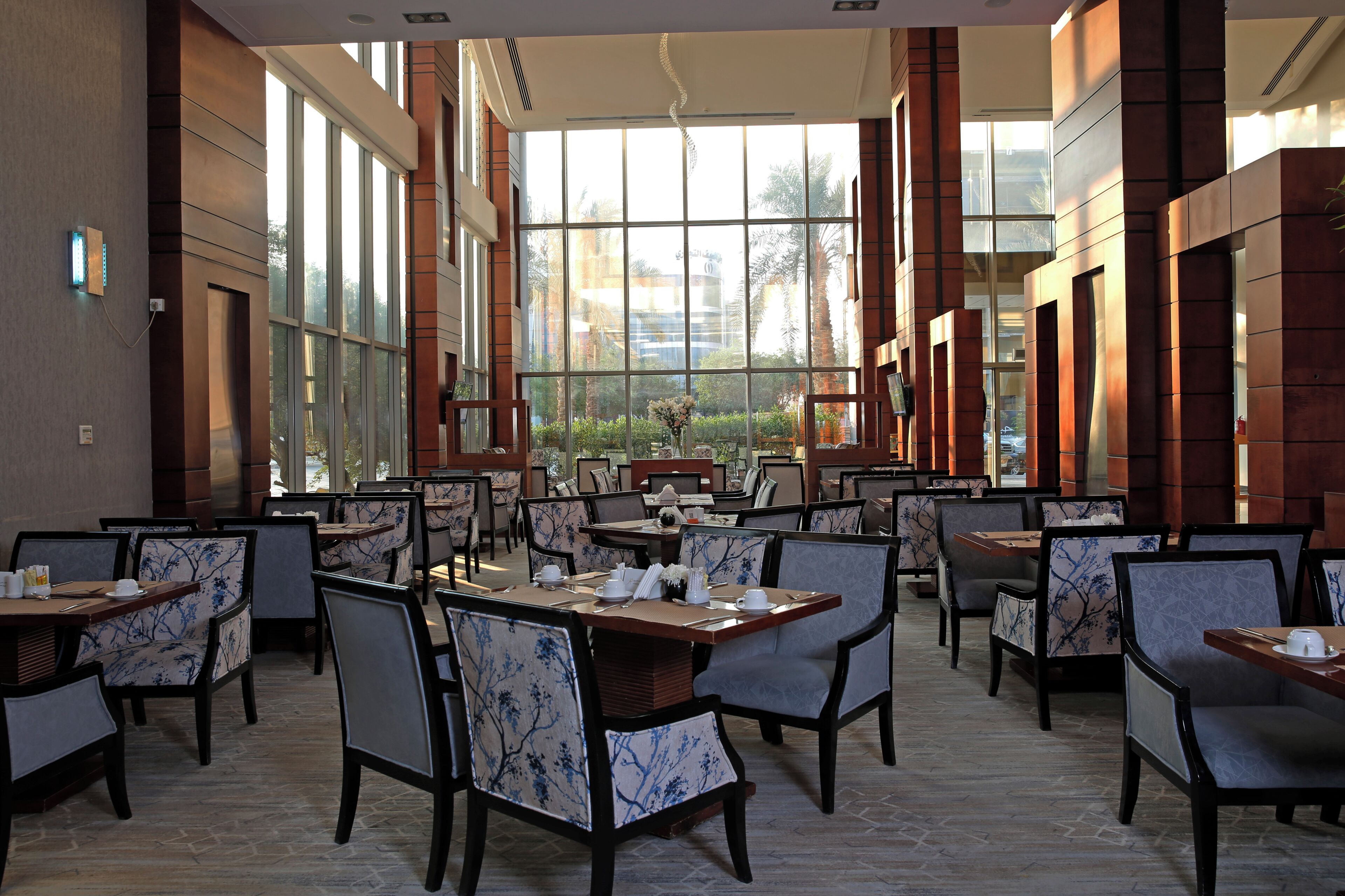 A spacious dining area with high ceilings and large windows, featuring modern furniture and a view of the outdoors.