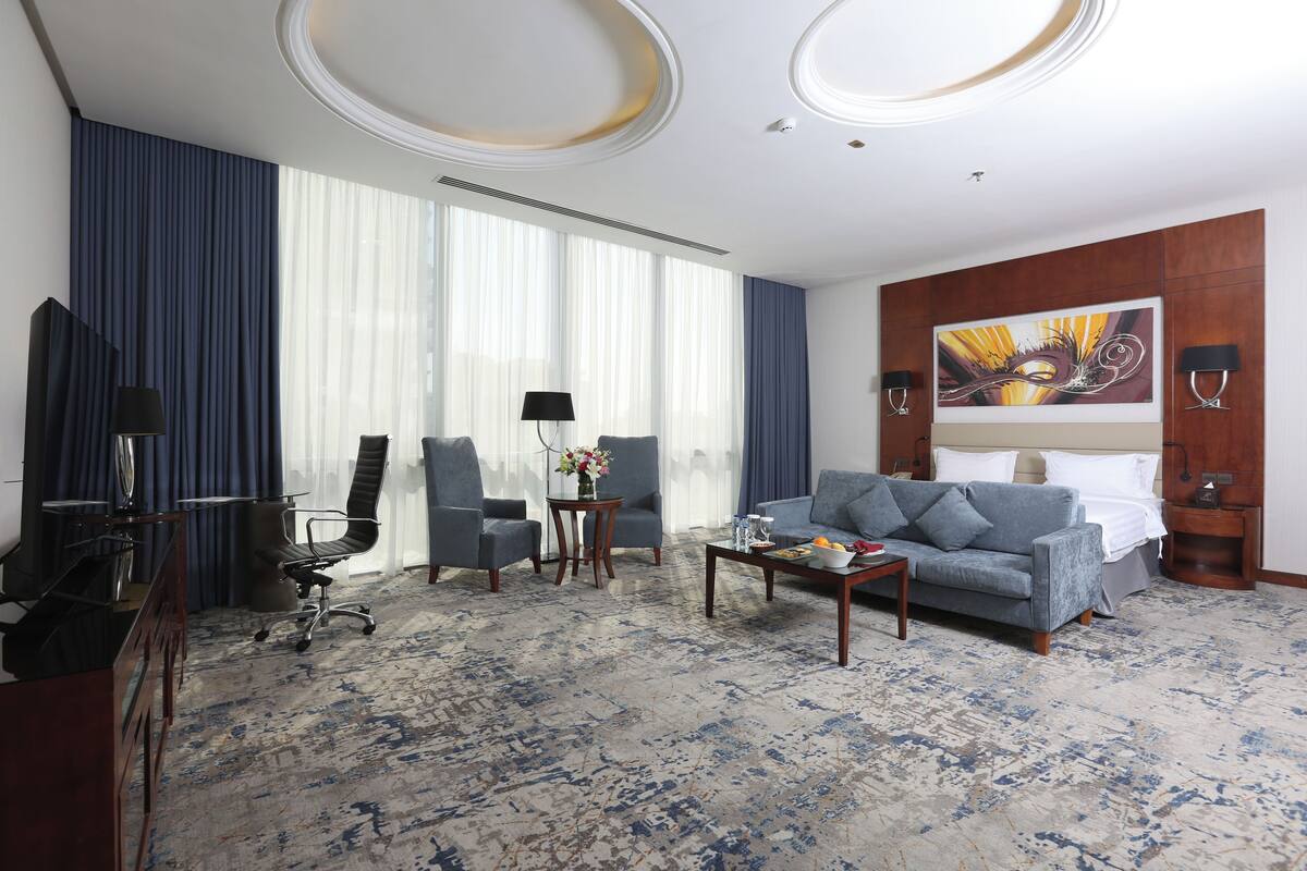 Quarto de hotel com uma cama grande, um sofá, uma escrivaninha, uma cadeira, uma mesa de centro e um quadro na parede.