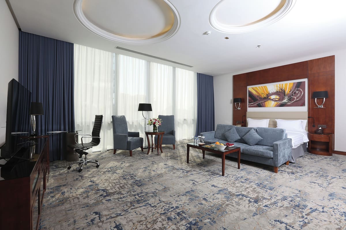 Une chambre d’hôtel avec un grand lit, un canapé, un bureau, une chaise, une table basse et un tableau au mur.