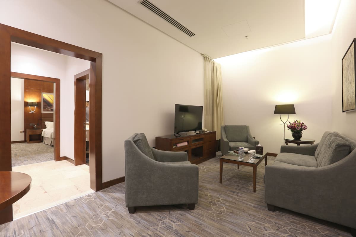 Une chambre d’hôtel avec deux fauteuils gris, un téléviseur, une table basse et une lampe.