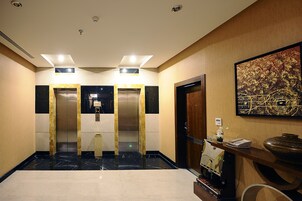 A hotel lobby with two elevators, a reception desk, and a large vase on the right.