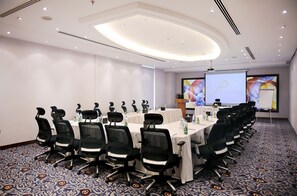 A conference room with a long table, black chairs, and a projector screen. - Qaser Alhamra Hotel Riyadh (Riyadh)