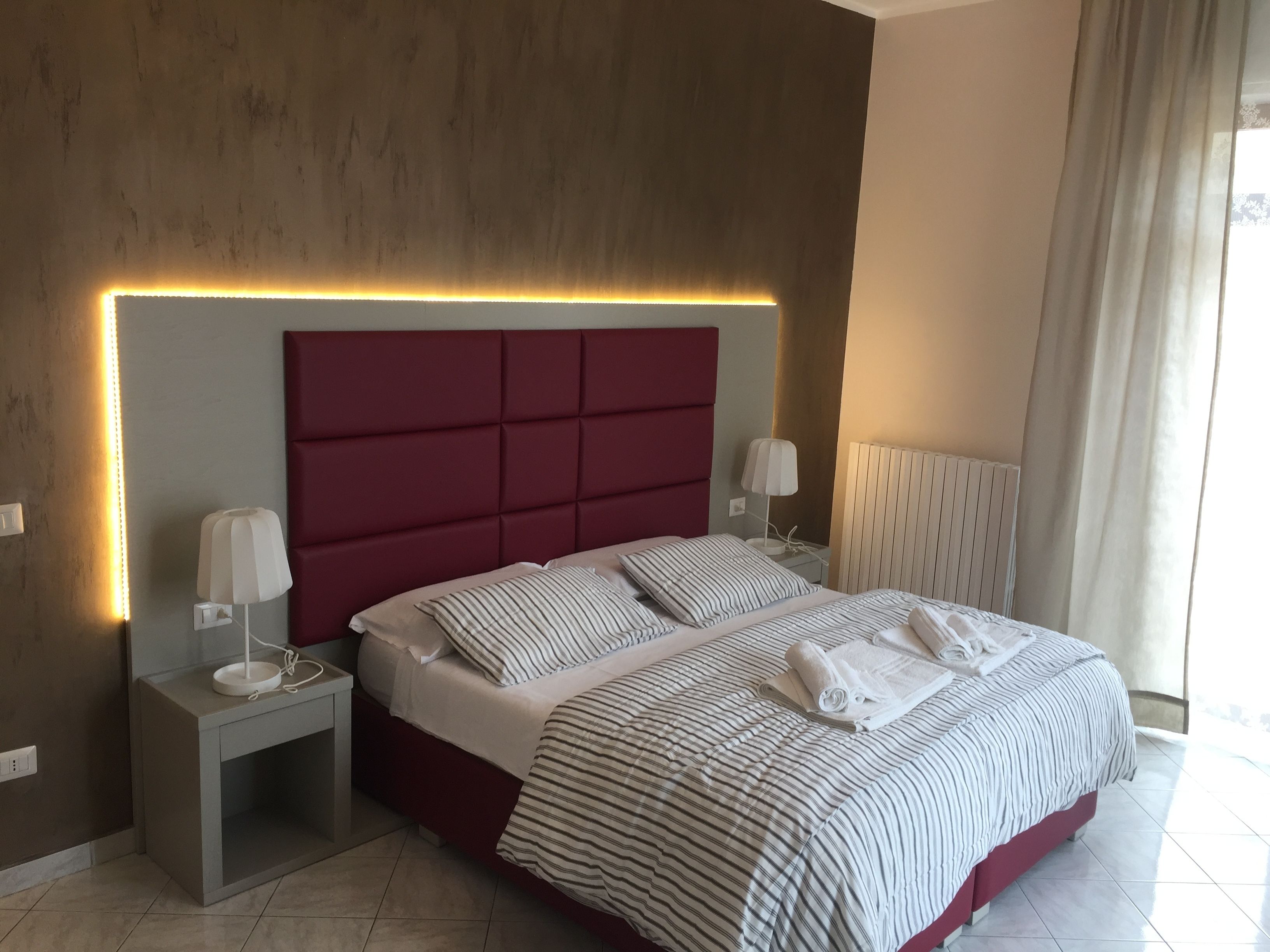 Una habitación de hotel moderna con una cama grande, una mesita de noche, una lámpara y un radiador.