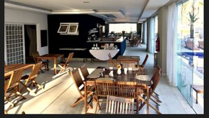 A modern dining area with wooden tables and chairs, a bar area, and large windows providing natural light. - Hotel Granja Brasil Resort (Petrópolis)