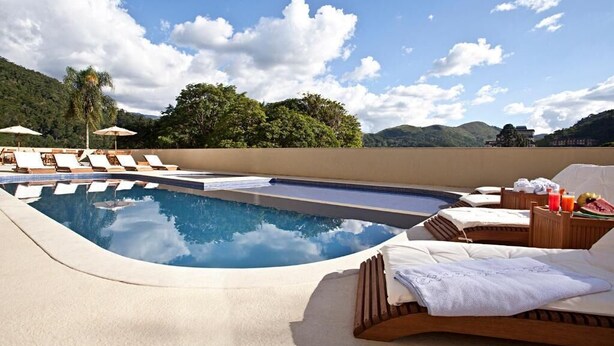 A pool area with lounge chairs, a small pool, and a bed with towels and a fruit basket. - Hotel Granja Brasil Resort (Petrópolis)